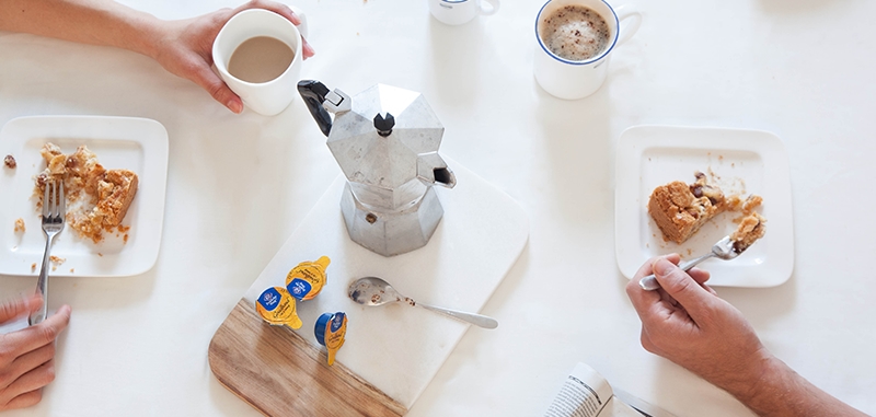 Foto van tafel waarop een percolator staat en mensen appeltaart eten.